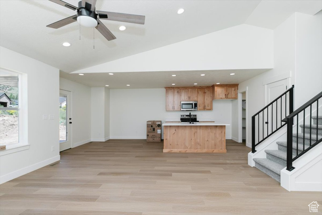 Kitchen with stainless steel microwave, range, light countertops, open floor plan, and a ceiling fan