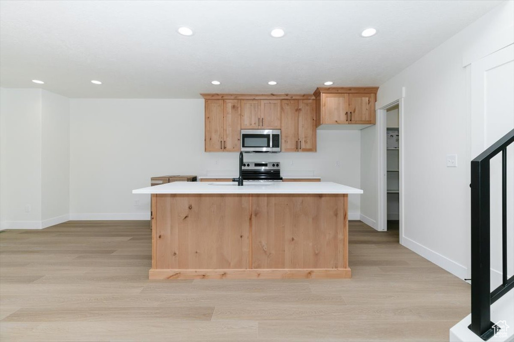 Kitchen with appliances with stainless steel finishes, light wood-style floors, light countertops, baseboards, and a center island