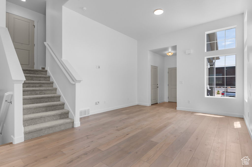 Unfurnished living room featuring light wood-type flooring, stairs, and baseboards