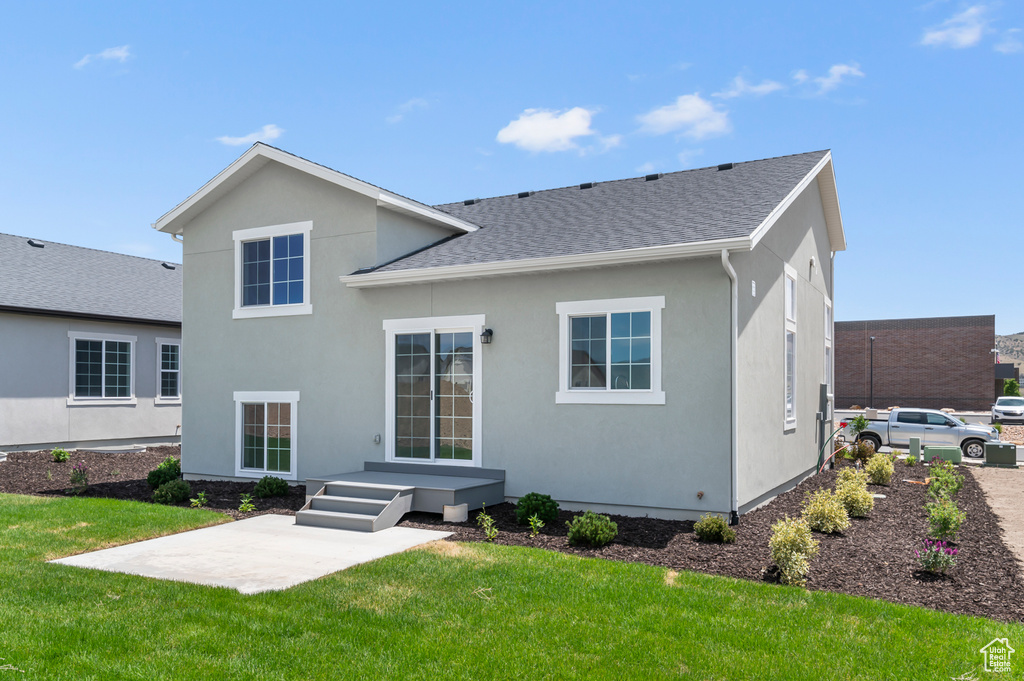 Rear view of property featuring roof with shingles, stucco siding, a yard, and a patio area