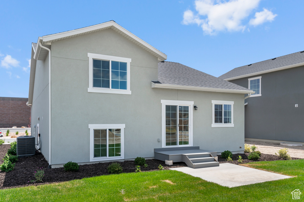 Back of property featuring central air condition unit, a lawn, stucco siding, and roof with shingles