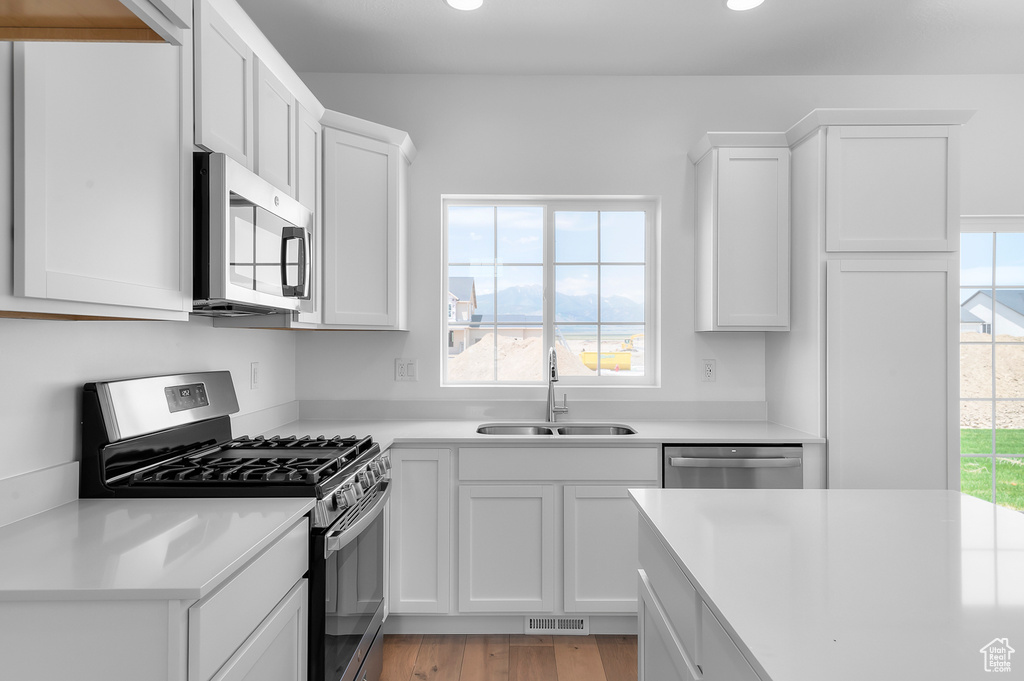 Kitchen featuring appliances with stainless steel finishes, a sink, white cabinets, light countertops, and light wood-style floors