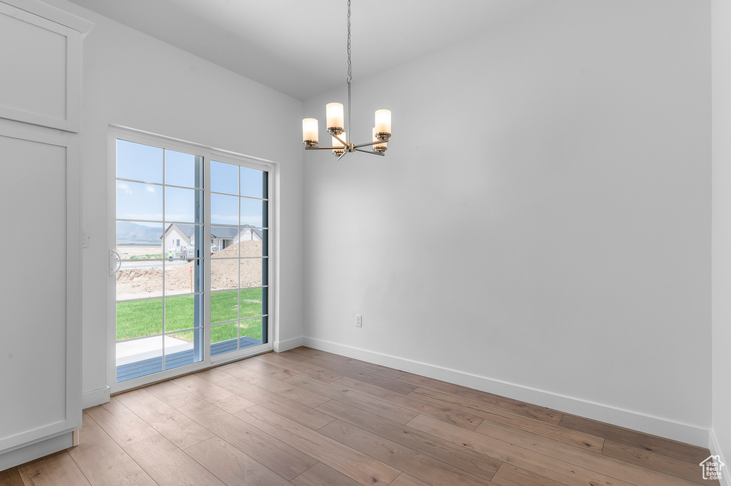 Empty room with a chandelier, baseboards, wood-type flooring, and plenty of natural light