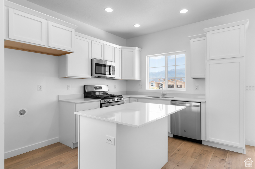 Kitchen with appliances with stainless steel finishes, a sink, light wood-type flooring, white cabinetry, and a kitchen island