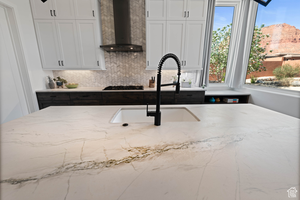 Kitchen featuring wall chimney range hood, black gas stovetop, light stone counters, and plenty of natural light