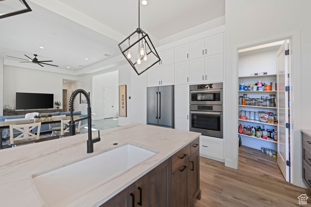 Kitchen featuring appliances with stainless steel finishes, a sink, light stone counters, light wood-type flooring, and decorative light fixtures