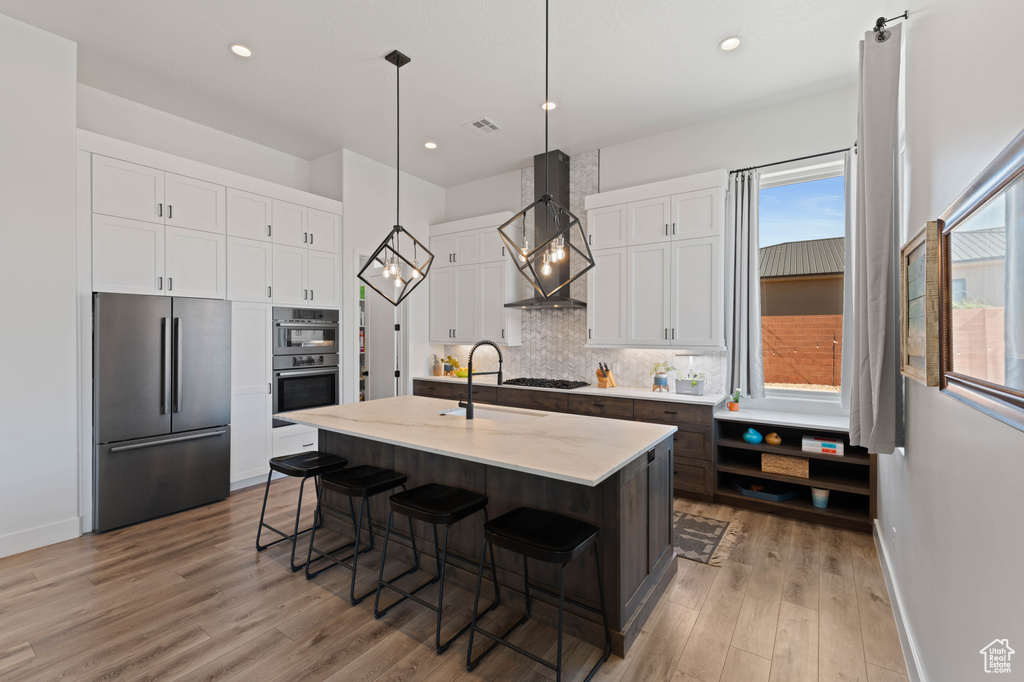 Kitchen featuring appliances with stainless steel finishes, wall chimney range hood, a sink, baseboards, and recessed lighting