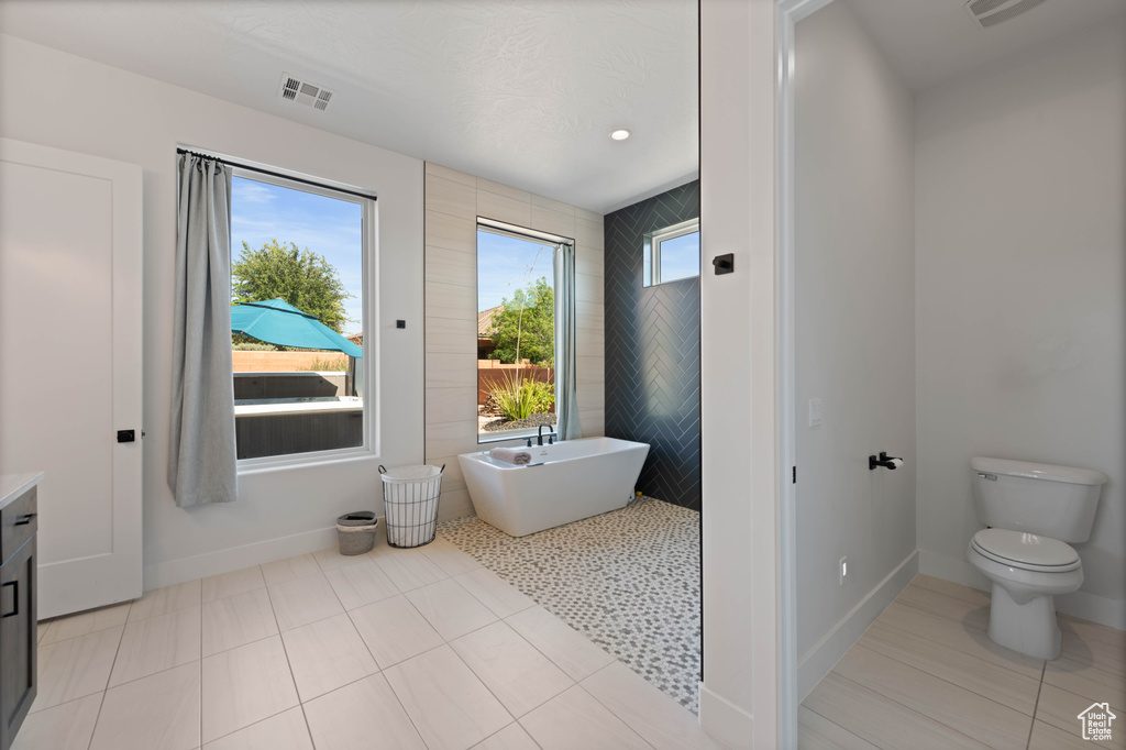 Full bathroom featuring toilet, a freestanding bath, vanity, tile patterned flooring, and baseboards