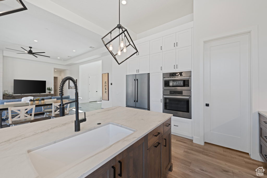 Kitchen featuring appliances with stainless steel finishes, a sink, wood finished floors, white cabinets, and decorative light fixtures
