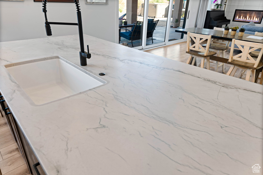 Detailed view of a sink, light wood finished floors, a glass covered fireplace, and light stone counters