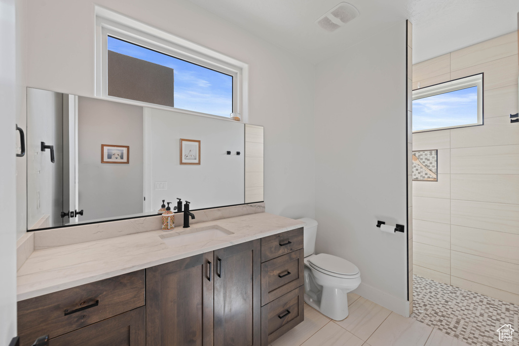 Full bath with tiled shower, toilet, vanity, and tile patterned flooring