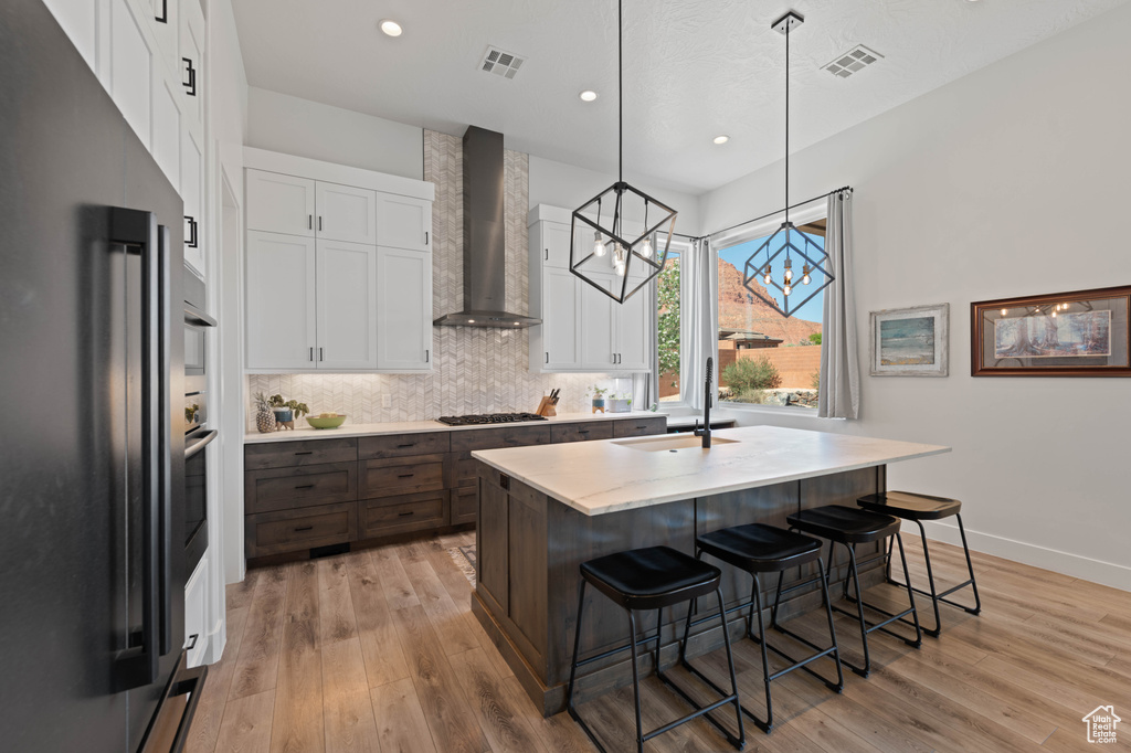 Kitchen featuring appliances with stainless steel finishes, a sink, wall chimney exhaust hood, white cabinets, and light wood-style flooring