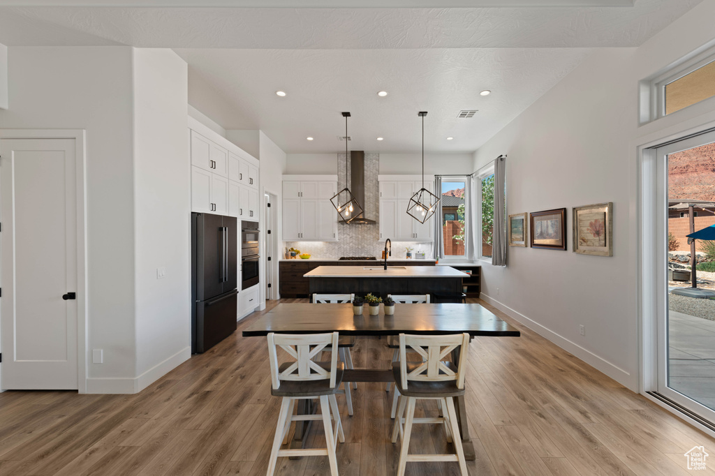 Kitchen featuring high quality fridge, wall chimney exhaust hood, baseboards, a kitchen island with sink, and recessed lighting