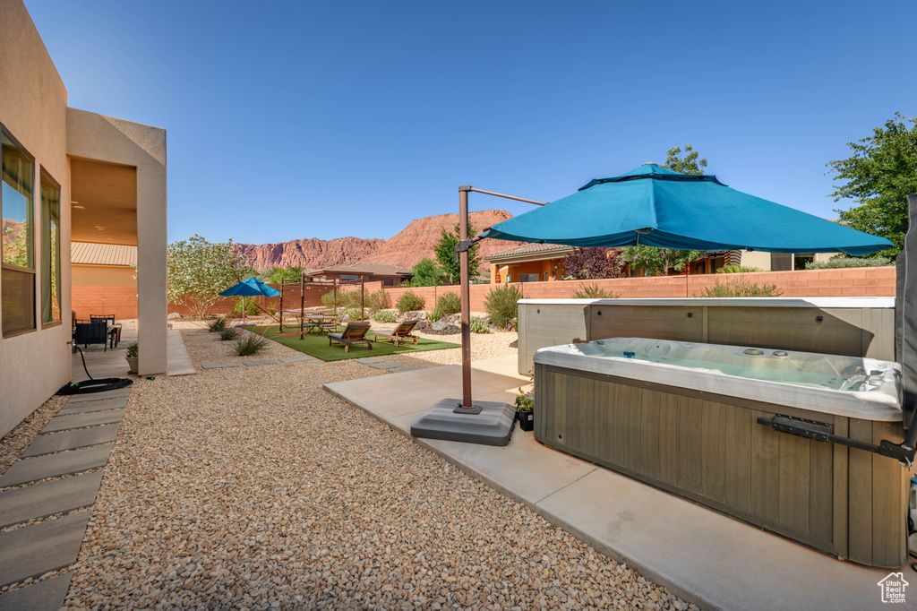 Fenced backyard with a hot tub, a mountain view, and a patio
