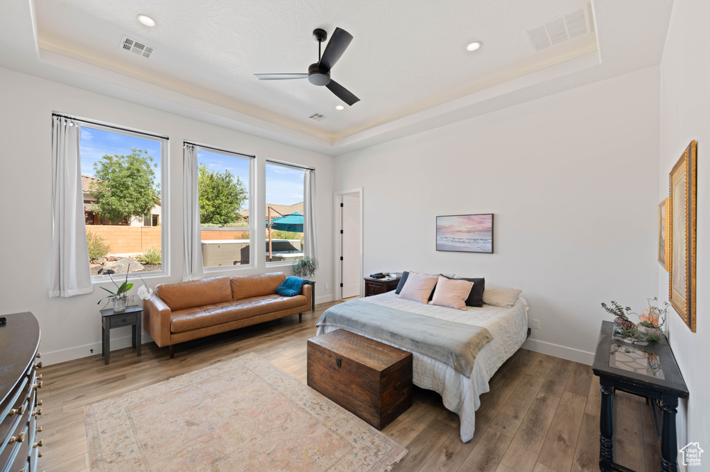 Bedroom with a tray ceiling, wood finished floors, baseboards, recessed lighting, and a ceiling fan