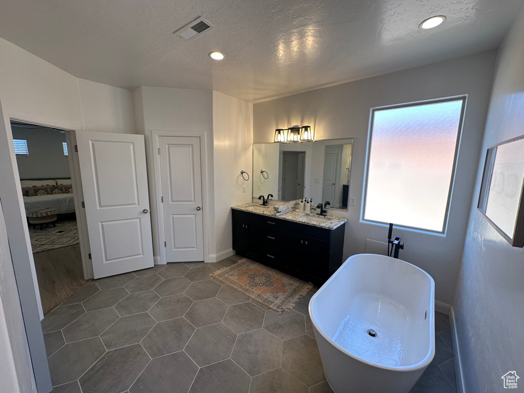 Ensuite bathroom featuring a freestanding bath, double vanity, recessed lighting, and tile patterned flooring