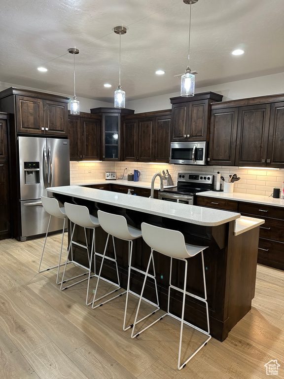 Kitchen with appliances with stainless steel finishes, a breakfast bar area, light countertops, decorative backsplash, and light wood-style flooring