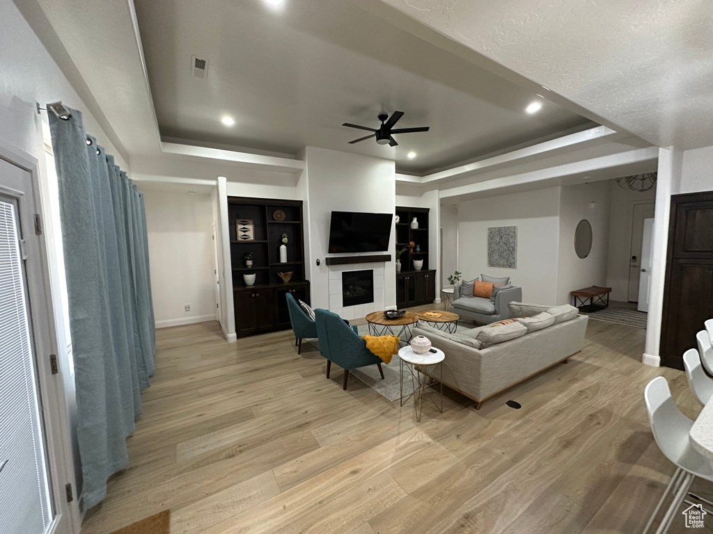 Living room featuring light wood-type flooring, ceiling fan, a tray ceiling, baseboards, and a fireplace