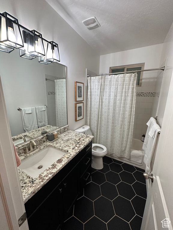Bathroom featuring vanity, toilet, shower / bath combo with shower curtain, tile patterned floors, and a textured ceiling