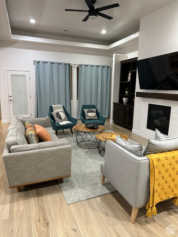 Living area with a tray ceiling, ceiling fan, wood finished floors, recessed lighting, and built in shelves