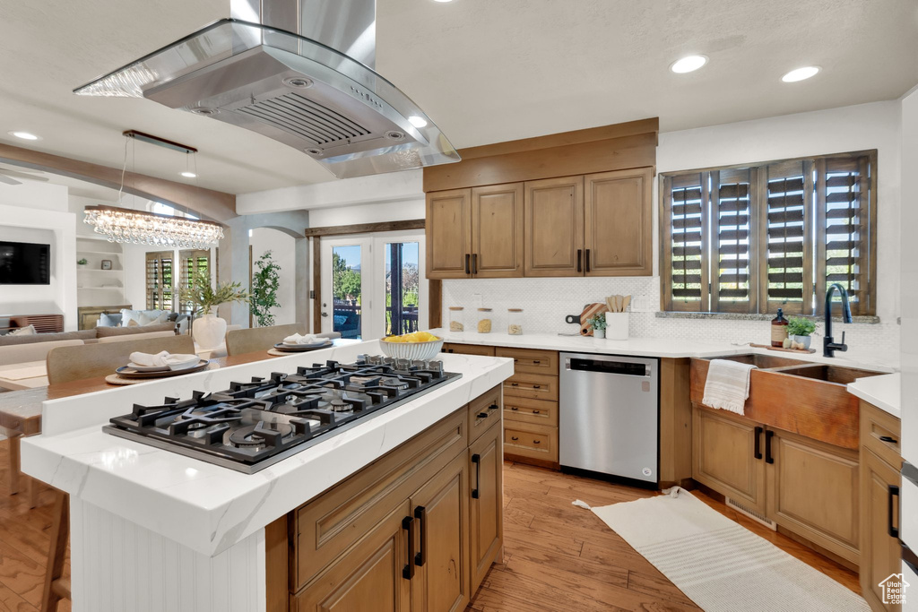Kitchen featuring dishwasher, range hood, gas cooktop, a sink, and light countertops