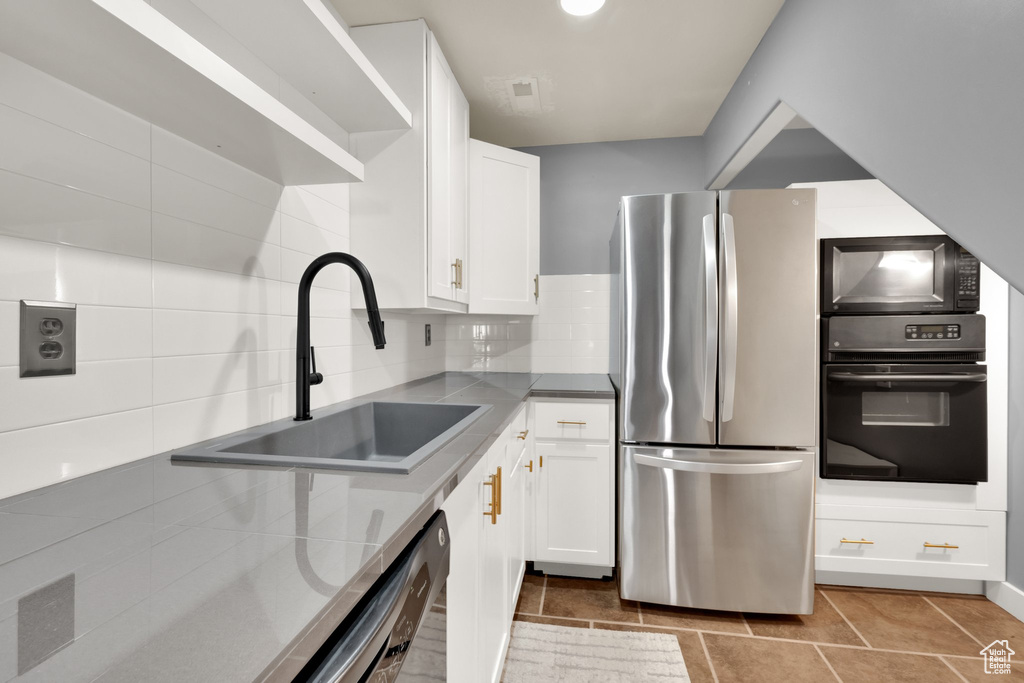 Kitchen featuring black appliances, a sink, white cabinets, decorative backsplash, and light tile patterned flooring