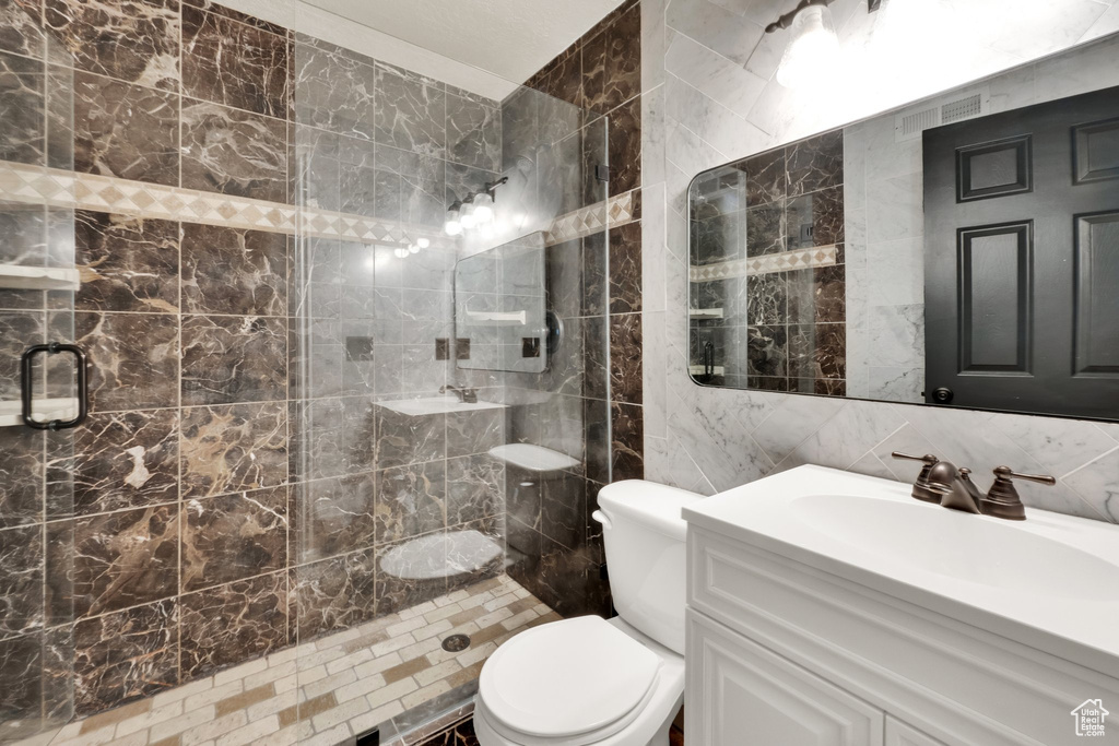 Bathroom featuring tile walls, a stall shower, vanity, and toilet