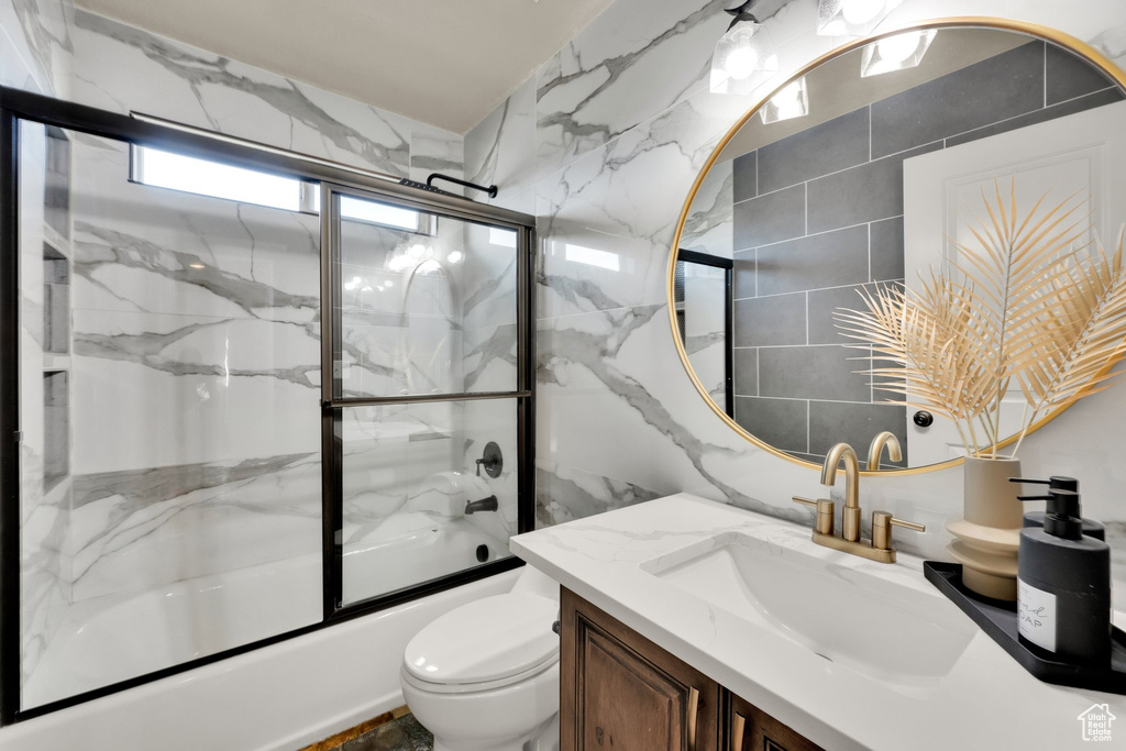Bathroom with vanity, combined bath / shower with glass door, toilet, and tile walls