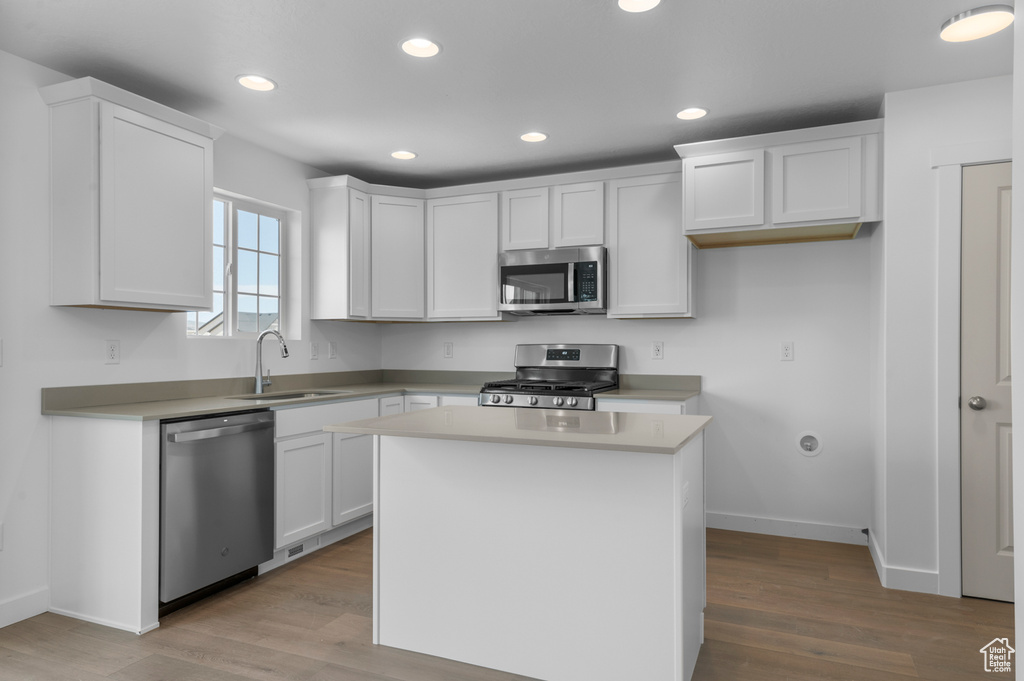 Kitchen with stainless steel appliances, a sink, light wood-style flooring, white cabinetry, and baseboards