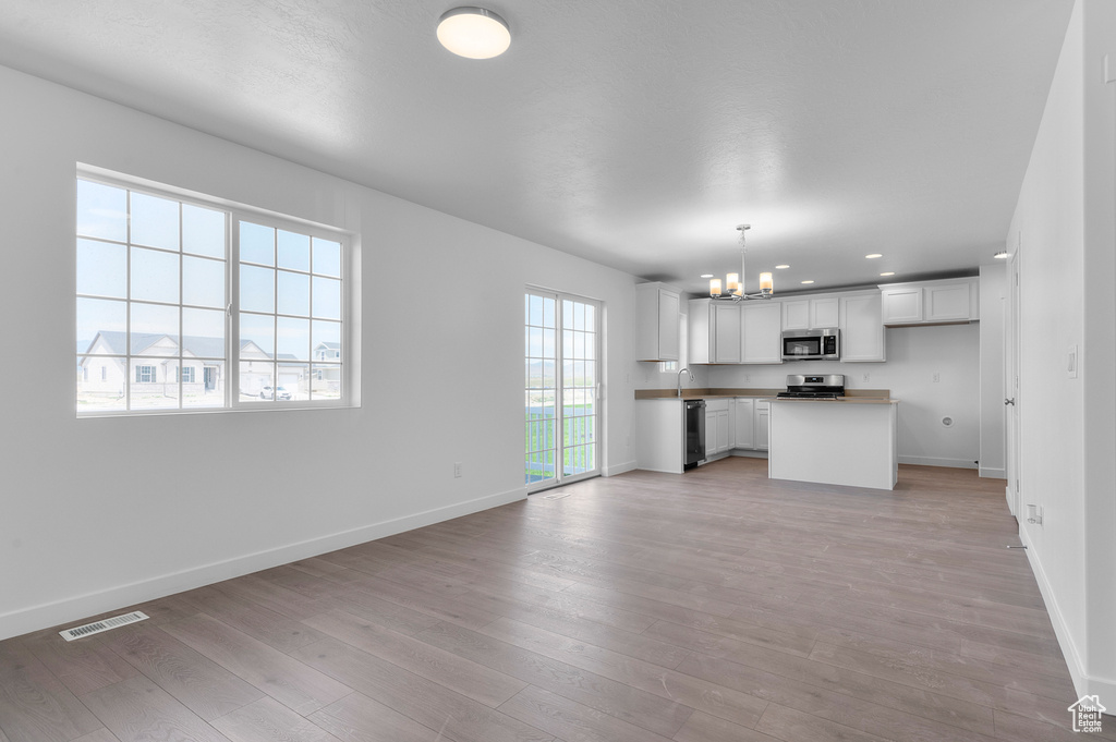 Kitchen featuring appliances with stainless steel finishes, a chandelier, open floor plan, baseboards, and light wood finished floors