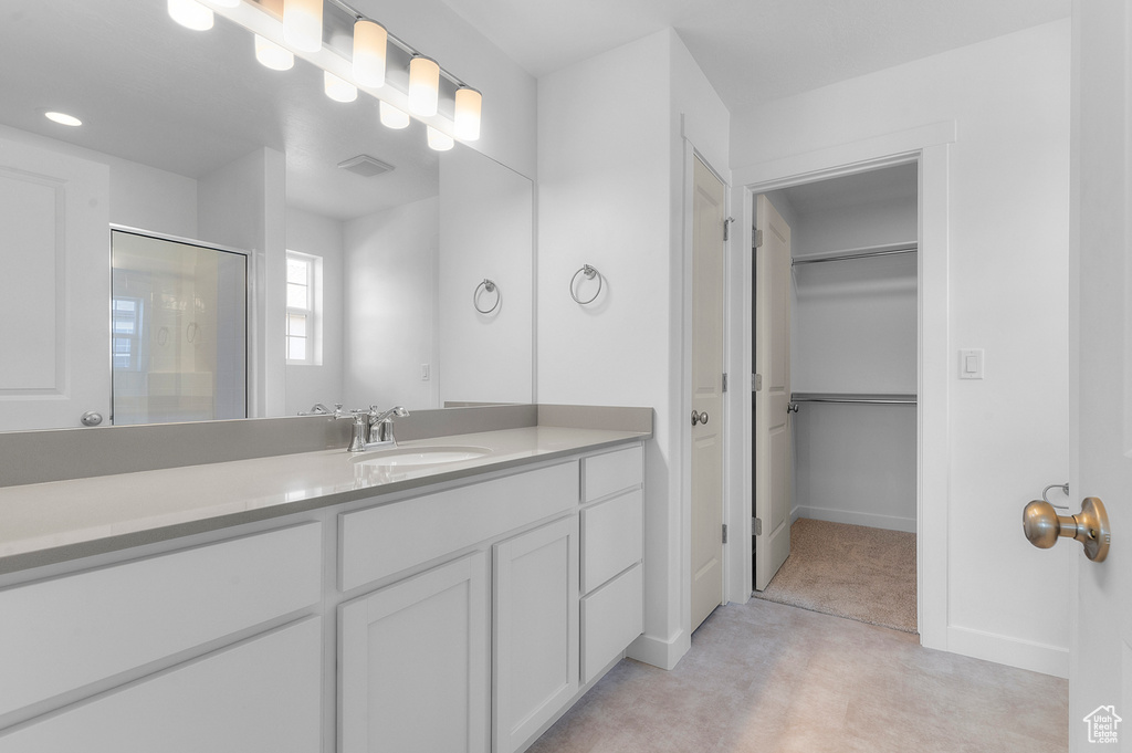 Full bathroom featuring vanity, a walk in closet, a shower with door, and baseboards
