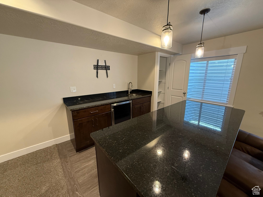 Kitchen with baseboards, a sink, dark brown cabinetry, dark stone countertops, and a textured ceiling