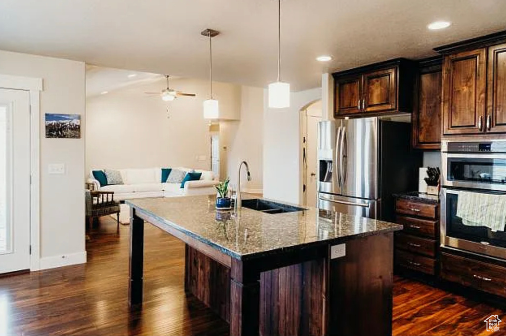 Kitchen with stainless steel appliances, a sink, dark wood finished floors, dark stone counters, and recessed lighting