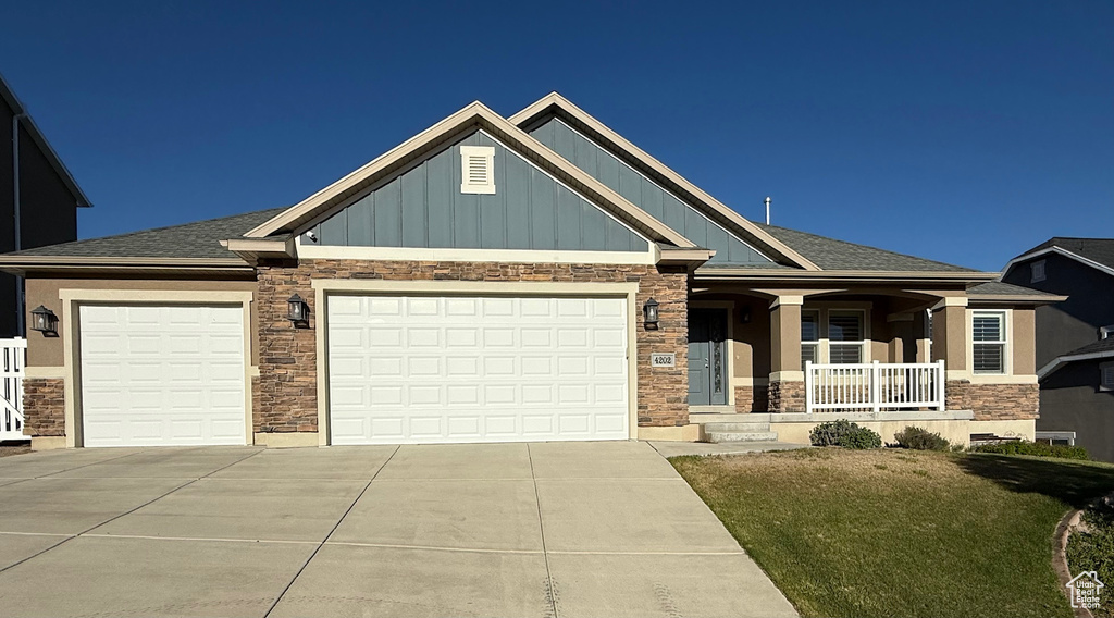 Craftsman-style home with stone siding, driveway, board and batten siding, covered porch, and an attached garage
