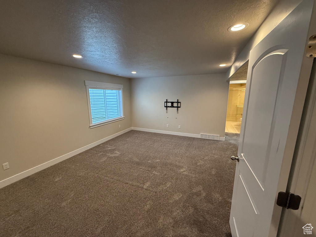 Empty room with a textured ceiling, recessed lighting, dark colored carpet, and baseboards