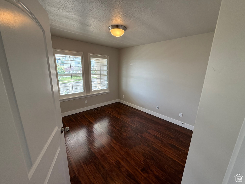 Empty room featuring a textured ceiling, baseboards, and dark wood finished floors