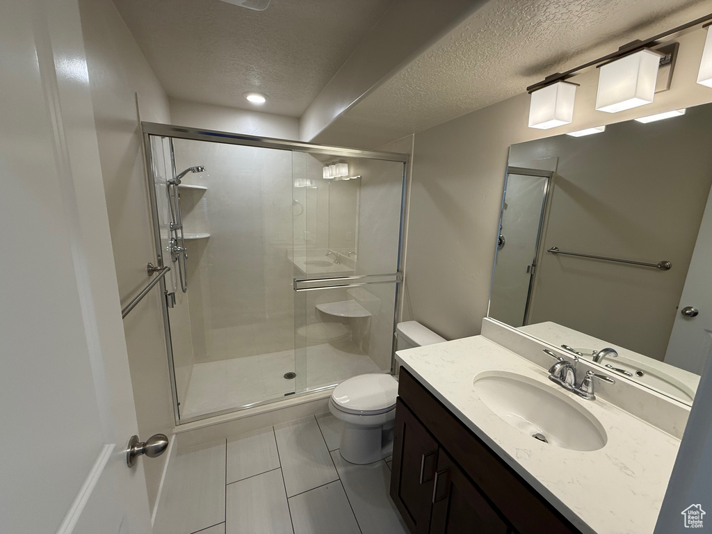 Bathroom featuring a textured ceiling, a stall shower, toilet, vanity, and tile patterned flooring