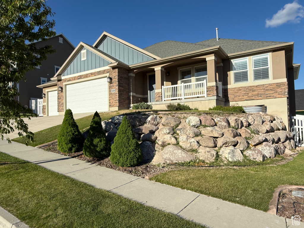 Craftsman-style home featuring stone siding, board and batten siding, covered porch, an attached garage, and a front yard