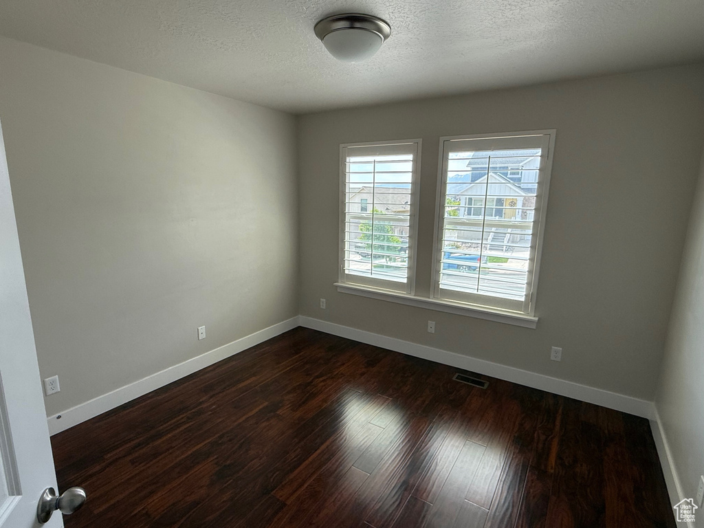 Spare room featuring dark wood-type flooring, baseboards, and a textured ceiling