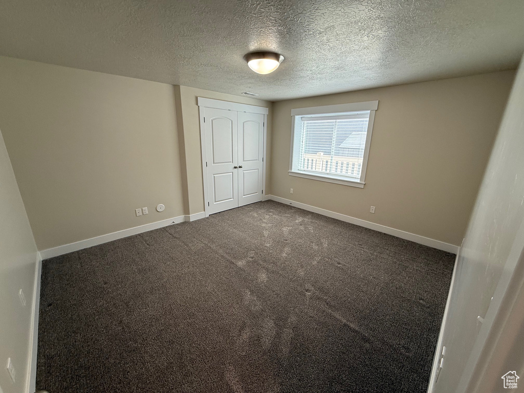 Unfurnished bedroom with a textured ceiling, baseboards, dark colored carpet, and a closet