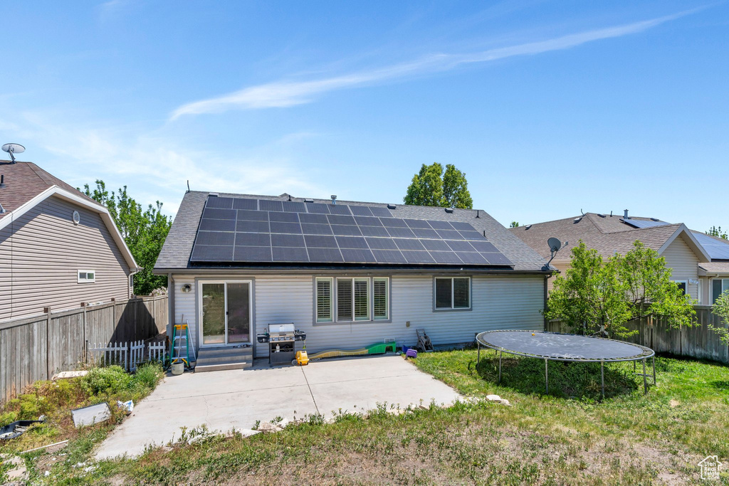 Back of house with a trampoline, a patio area, solar panels, and a fenced backyard