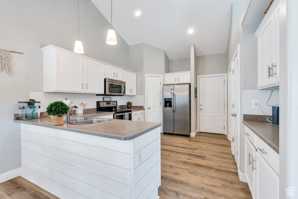 Kitchen featuring appliances with stainless steel finishes, a sink, a peninsula, decorative backsplash, and high vaulted ceiling