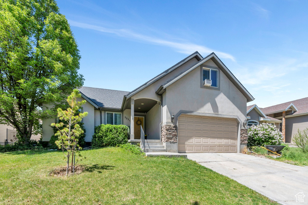 View of front of house featuring stucco siding, concrete driveway, a front yard, and an attached garage
