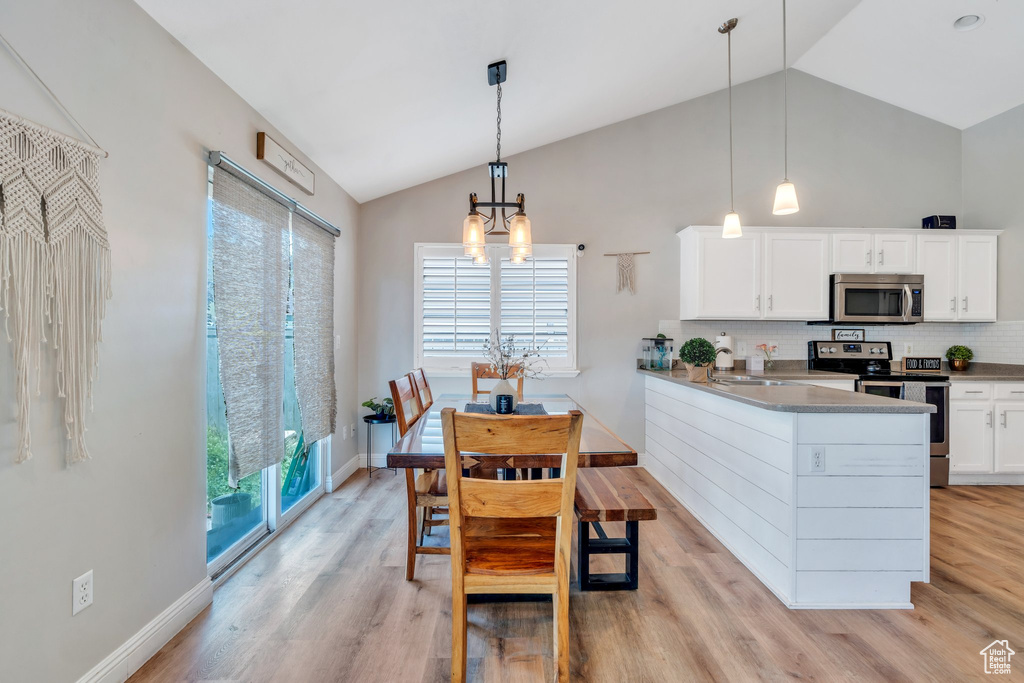 Kitchen with stainless steel appliances, white cabinets, a chandelier, decorative backsplash, and light wood-style floors