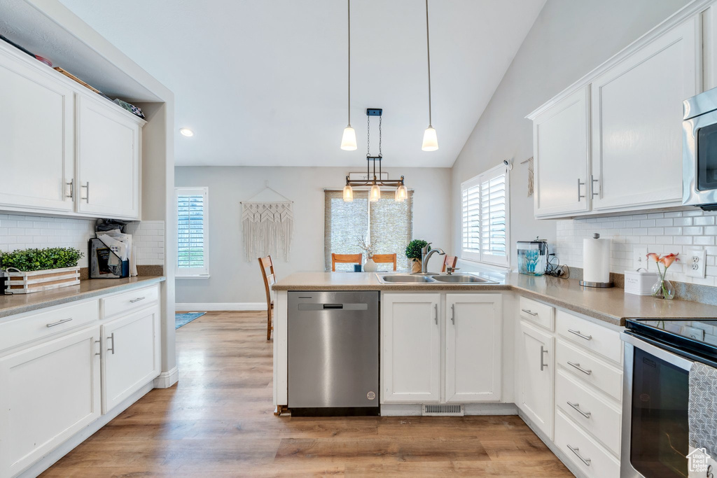 Kitchen featuring appliances with stainless steel finishes, a sink, a peninsula, white cabinetry, and vaulted ceiling