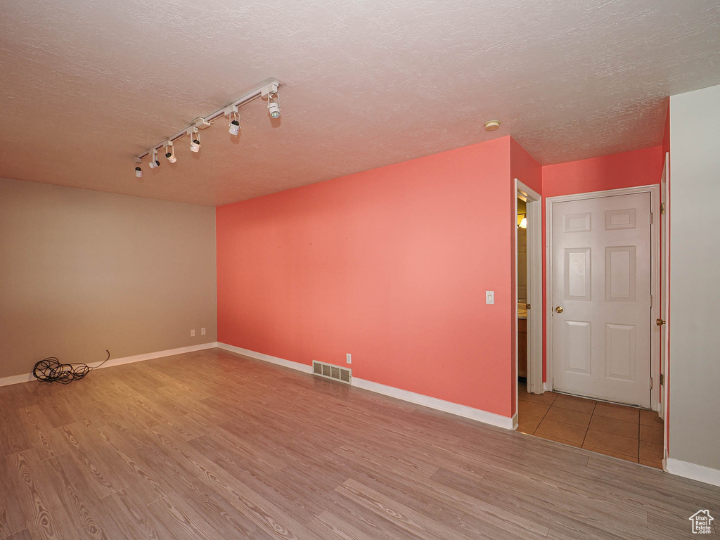 Empty room featuring track lighting, wood finished floors, a textured ceiling, and baseboards