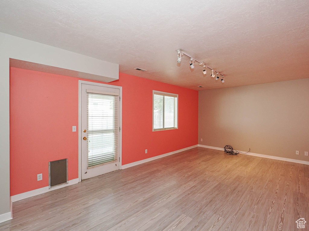 Unfurnished room with track lighting, light wood-style flooring, baseboards, and a textured ceiling