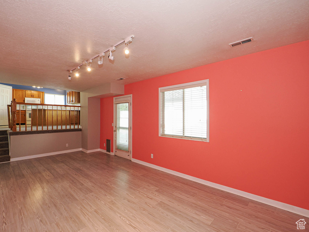 Unfurnished living room with a textured ceiling, light wood-type flooring, baseboards, and track lighting