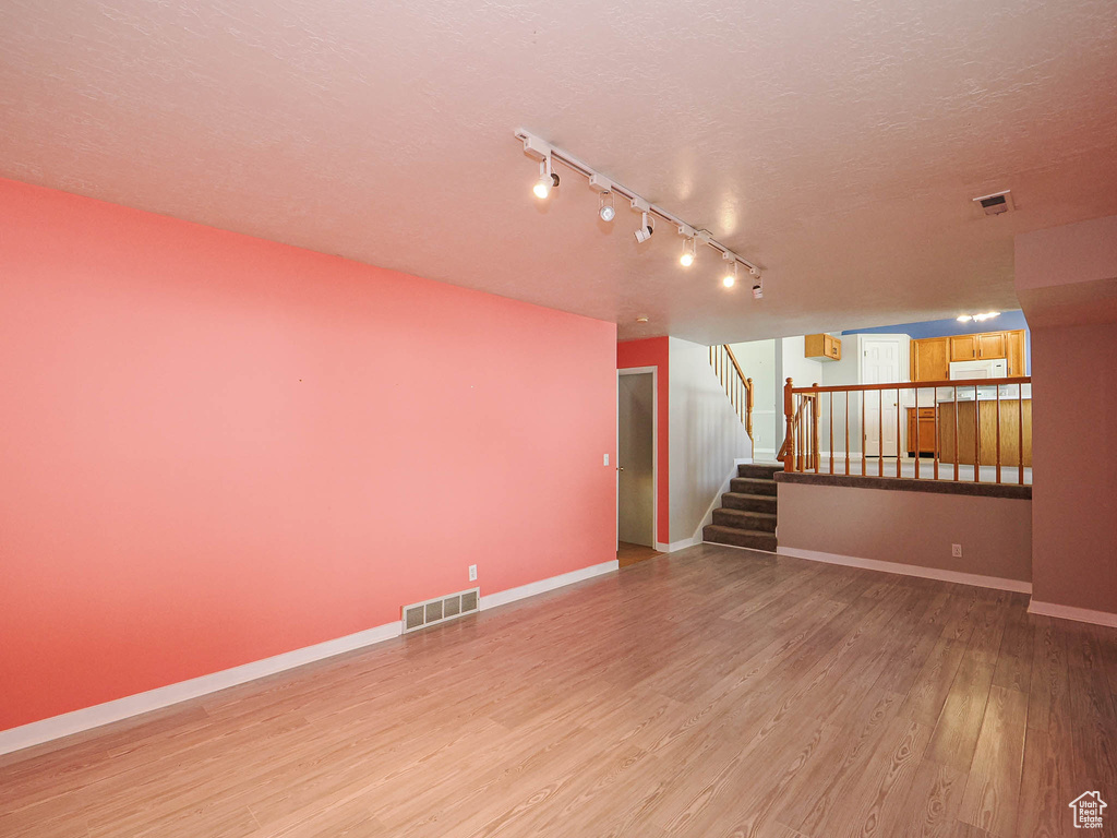 Unfurnished living room featuring light wood-style floors, a textured ceiling, baseboards, stairway, and track lighting