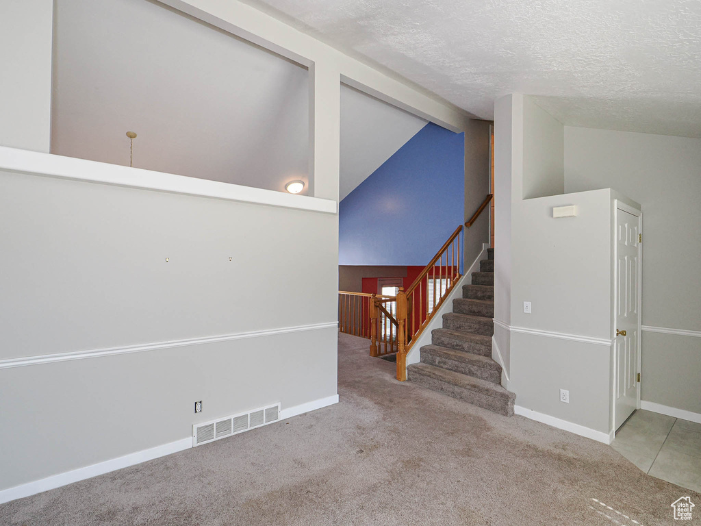 Unfurnished living room featuring carpet floors, a textured ceiling, stairway, high vaulted ceiling, and baseboards